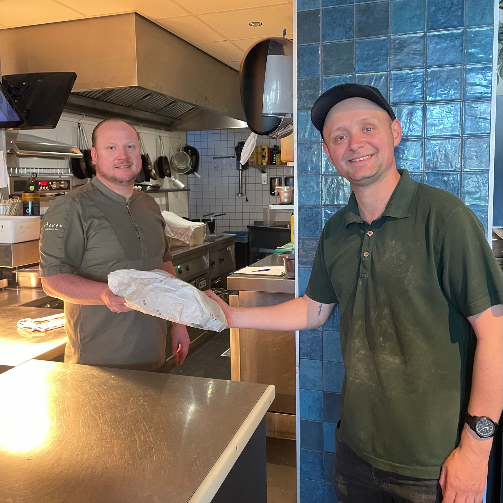 Fietskoerier Davy overhandigt versgebakken brood aan de chef in de keuken van restaurant steven in Nijmegen.